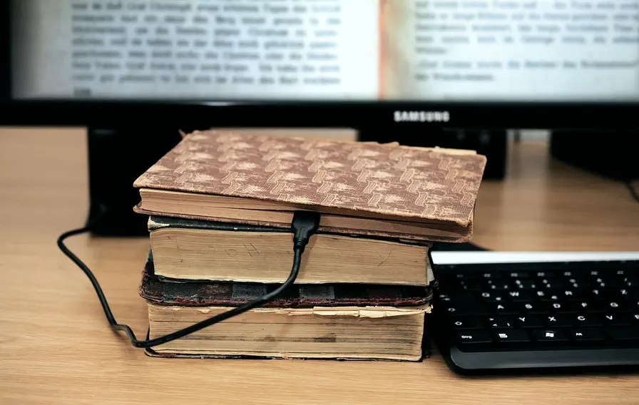 Alte Bücher digitalisiert: Symbol für digitale Transformation, Smart Water Management und modernes Wissensmanagement in Deutschland. Stapel alter Bücher mit angeschlossenem Kabel vor einem Monitor und einer Tastatur, symbolisiert digitale Transformation und Wissensmanagement in Deutschland.